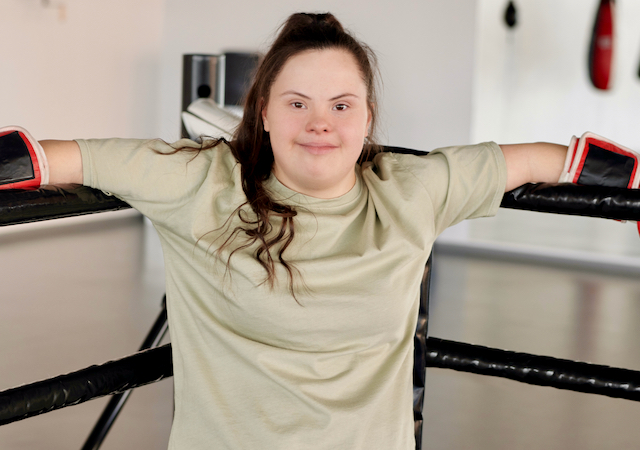 Young woman with Down Syndrome smiling in a boxing ring. Photo by Cliff Booth, from Pexels