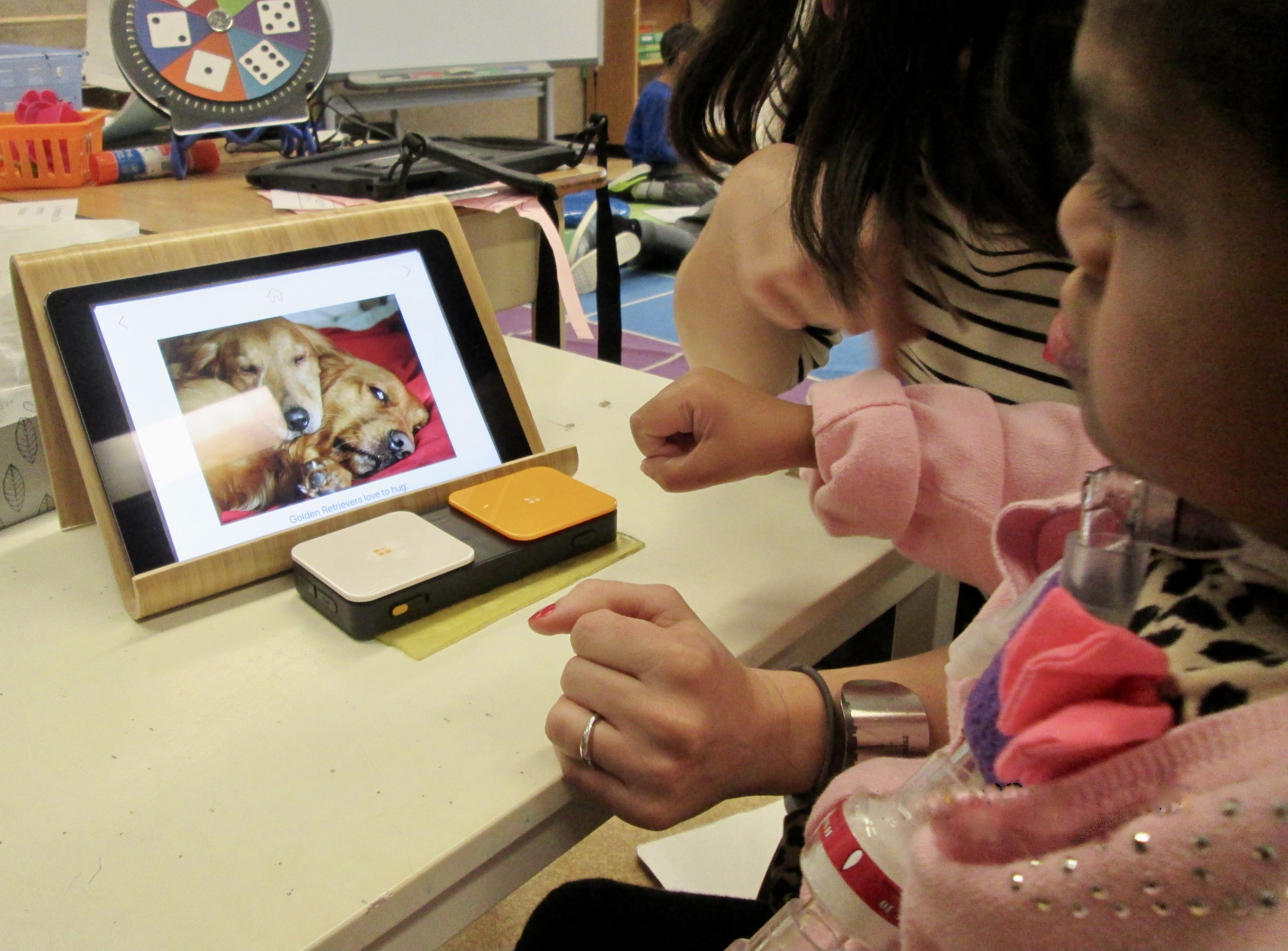 Student on the Pictello app on an iPad. A Bluetooth Switch is on the desk for her to use to turn the pages