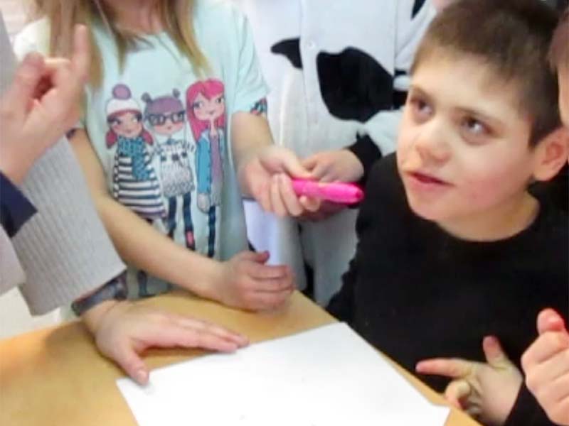 A student holds a scented marker next to her classmate's nose, while the educator assists.